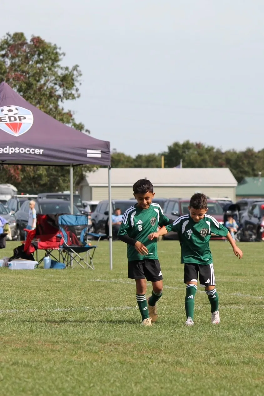 Two EKS teammates in green walking off the field together, arm in arm, at the EDP Fall Cup